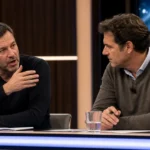 Twee analisten in een televisiestudio tijdens een voetbaldiscussie aan een desk.