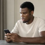 Raphael Onyedika in neutrale kleding terwijl hij op zijn smartphone kijkt.