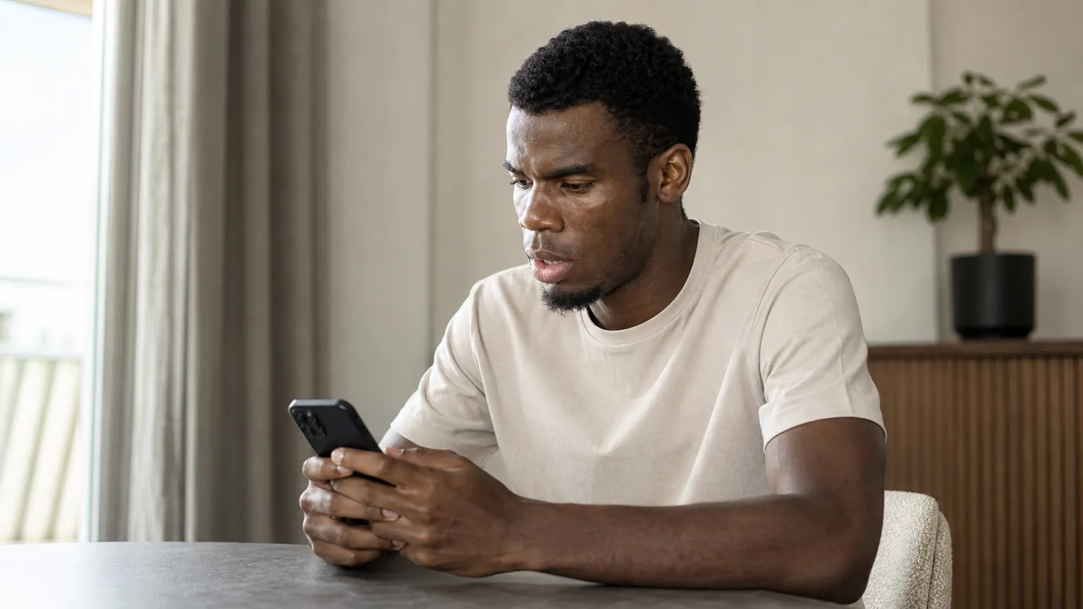 Raphael Onyedika in neutrale kleding terwijl hij op zijn smartphone kijkt.