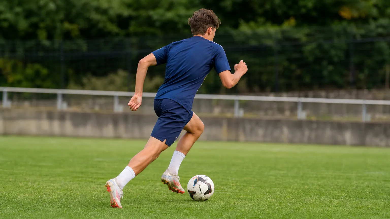 Een niet-identificeerbare jonge voetballer dribbelt met de bal op een grasveld.