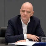 Gianni Infantino zit aan een vergadertafel in een FIFA-conferentieruimte.