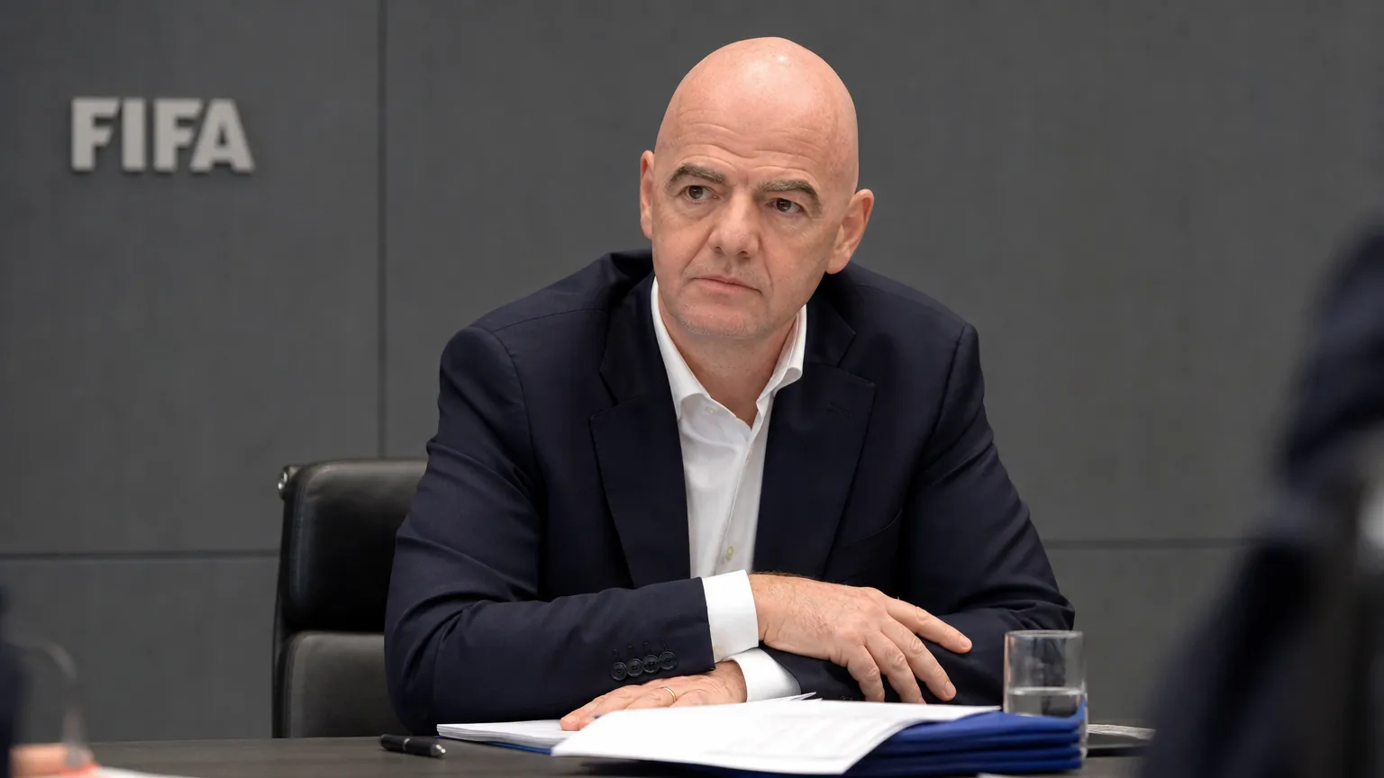 Gianni Infantino zit aan een vergadertafel in een FIFA-conferentieruimte.