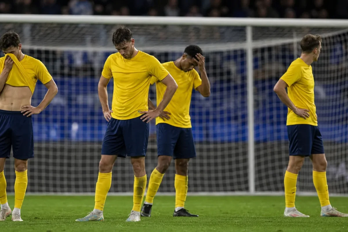 Teleurgestelde voetballers in gele shirts staan na een wedstrijd voor het doelnet.