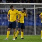 Teleurgestelde voetballers in gele shirts staan na een wedstrijd voor het doelnet.