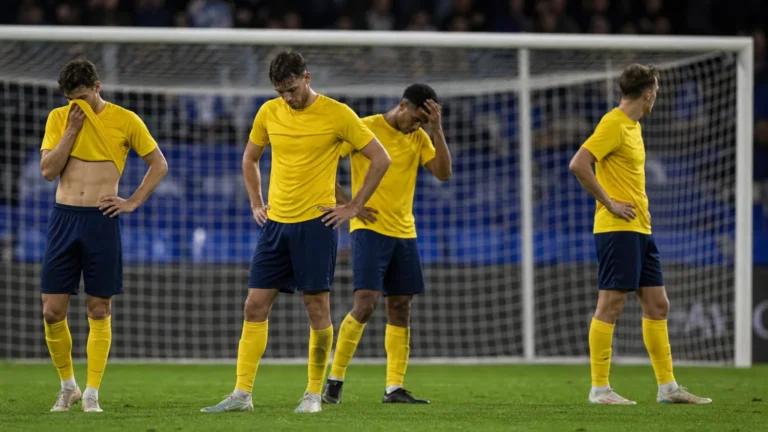 Teleurgestelde voetballers in gele shirts staan na een wedstrijd voor het doelnet.
