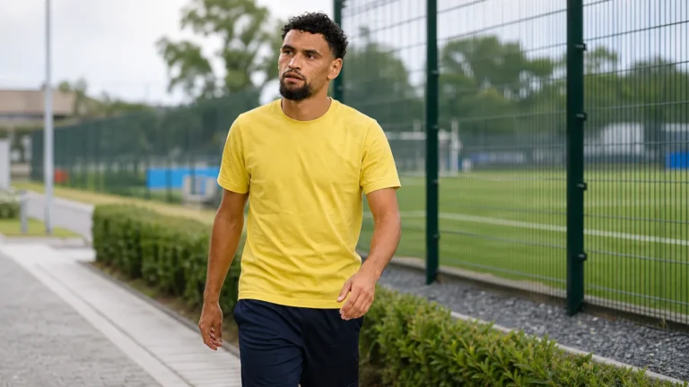 Adem Zorgane wandelt in neutrale sportkleding langs een voetbalcomplex.