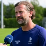 Rik De Mil spreekt in een interviewzone naast een voetbalveld.