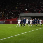 Een hoekschop wordt in een voetbalstadion richting het strafschopgebied getrapt.