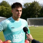 Dani van den Heuvel beantwoordt een vraag naast een voetbalveld.