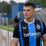 Een Club Brugge-speler in blauw-zwart kijkt geconcentreerd naast het veld.