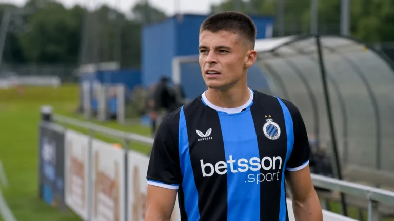Een Club Brugge-speler in blauw-zwart kijkt geconcentreerd naast het veld.