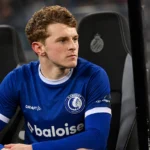 Max Dean in het blauwe shirt van KAA Gent op de spelersbank tijdens een avondwedstrijd.