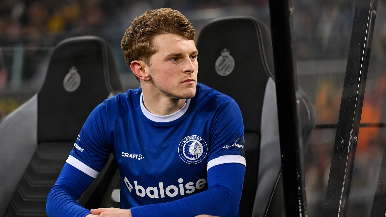 Max Dean in het blauwe shirt van KAA Gent op de spelersbank tijdens een avondwedstrijd.
