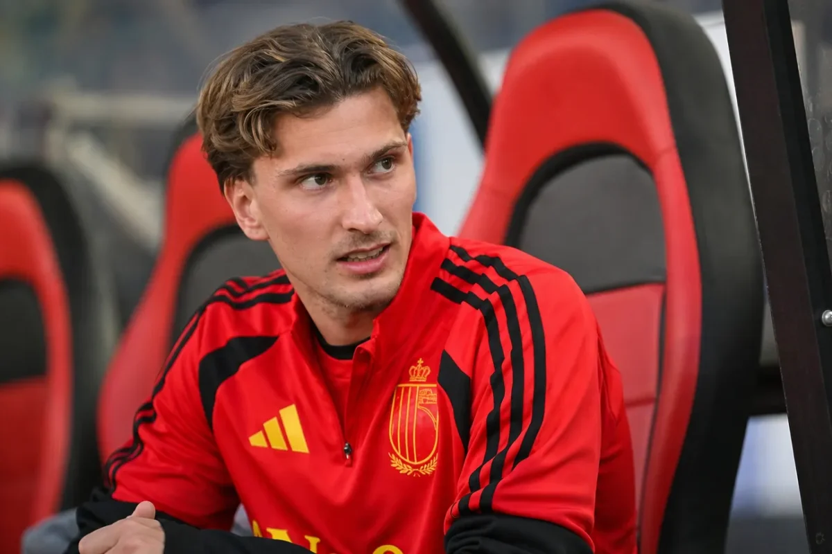 Mika Godts in een rood shirt in de dug-out van een stadion.