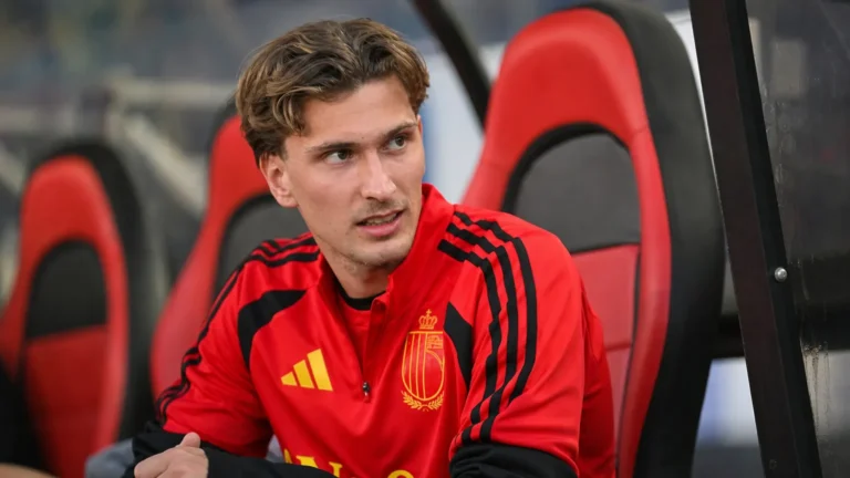 Mika Godts in een rood shirt in de dug-out van een stadion.