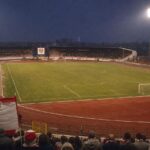 Het historische Regenboogstadion van KSV Waregem met atletiekpiste, rood-witte accenten en supporters op de achtergrond.
