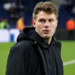 Leo Hjelde in zwarte sportieve bovenkleding langs de rand van een voetbalveld.