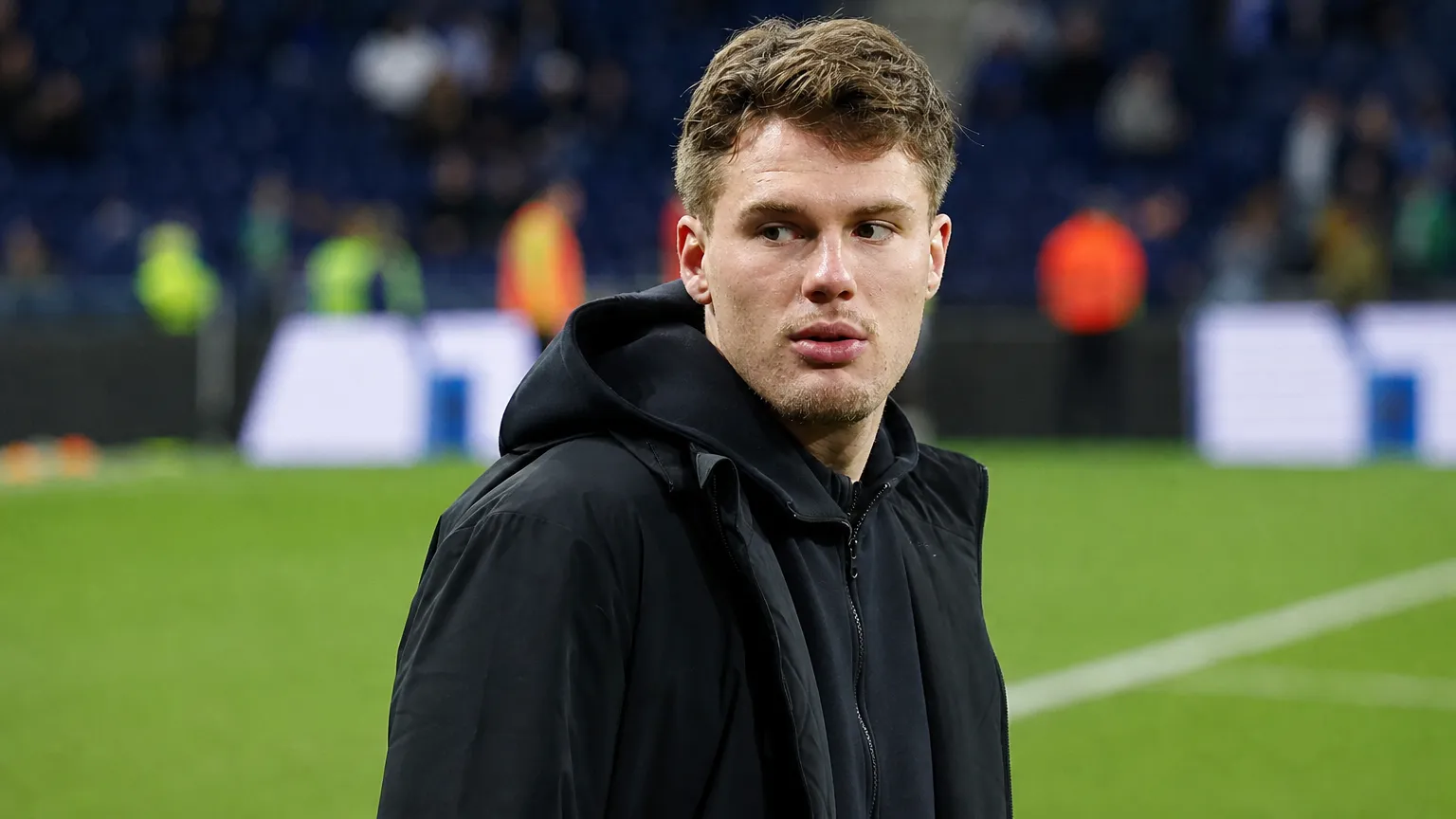 Leo Hjelde in zwarte sportieve bovenkleding langs de rand van een voetbalveld.