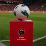 Een wedstrijdbal op een rode sokkel van de Jupiler Pro League langs het veld.