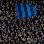 Supporters van Club Brugge in het stadion met een blauw-zwarte vlag.