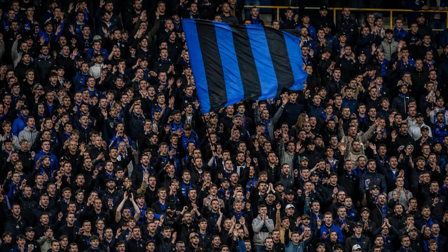 Supporters van Club Brugge in het stadion met een blauw-zwarte vlag.