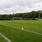 Leeg trainingsveld bij het trainingscomplex van KRC Genk met een discreet clubbord.