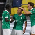 Drie spelers van Lommel SK in groene wedstrijdshirts bij de rand van het veld.