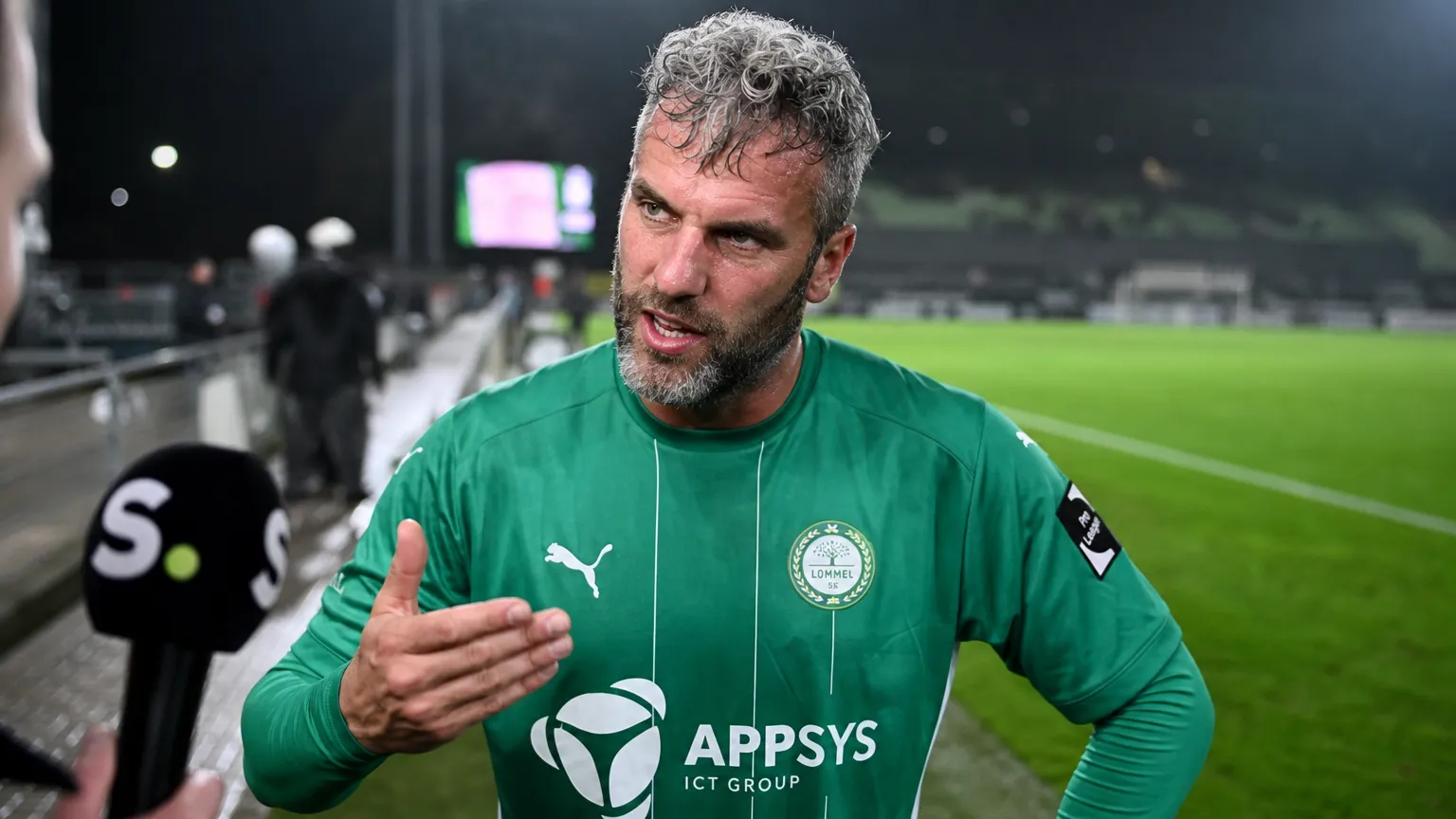 Ralf Seuntjens in groen voetbalshirt tijdens een gesprek naast het veld.