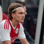 Mika Godts zit op de reservebank in zijn wit-rode Ajax-tenue.