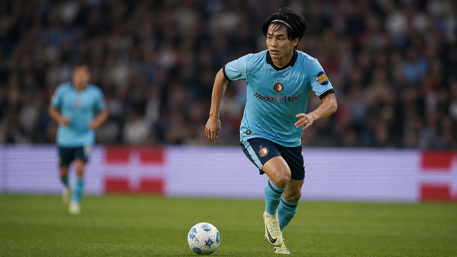 Ayase Ueda in een lichtblauw Feyenoord-shirt tijdens een voetbalactie op het veld.