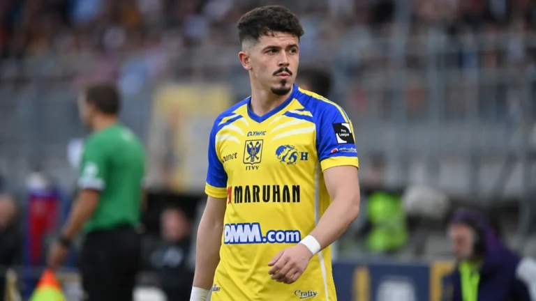 Arbnor Muja in het geel-blauwe tenue van STVV langs de zijlijn van een voetbalveld.
