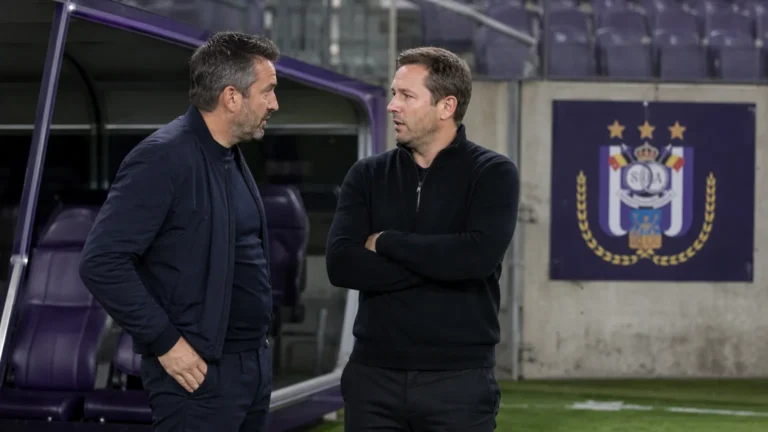 Neutrale medewerkers in de technische zone van een stadion met een discreet Anderlecht-bord op de achtergrond.