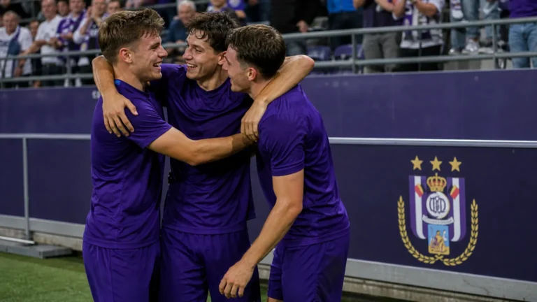 Drie voetballers in paarse uitrusting vieren samen voor een discreet RSC Anderlecht-bord.