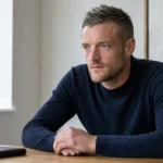 Jamie Vardy zit in neutrale kleding aan een tafel in een rustige binnenruimte.
