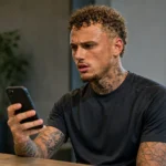 Noa Lang kijkt naar zijn smartphone in een rustige binnenruimte.