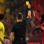 Scheidsrechter heft geel terwijl protesterende spelers druk zetten