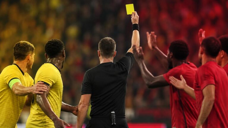Scheidsrechter heft geel terwijl protesterende spelers druk zetten
