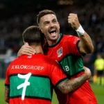 Twee voetballers vieren samen op het veld na een late treffer.