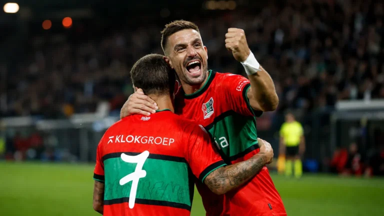 Twee voetballers vieren samen op het veld na een late treffer.