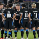 Club Brugge-spelers vormen een hechte kring op het veld in zwarte wedstrijdtenues.