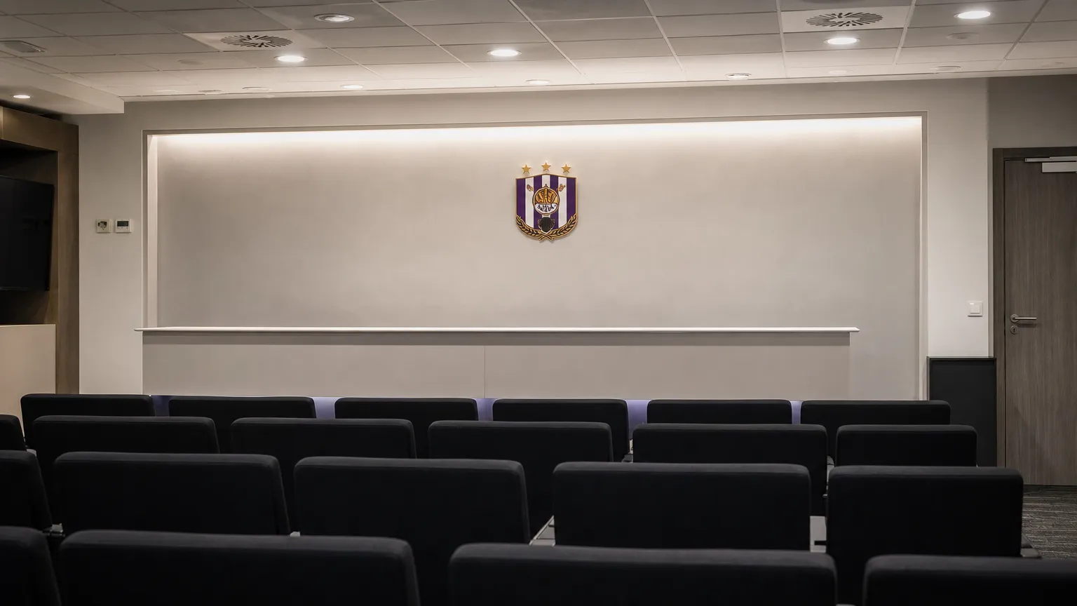 Rustige persruimte met een discreet RSC Anderlecht-embleem op de wand.