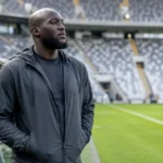 Romelu Lukaku in neutrale sportkleding aan de rand van een voetbalveld.