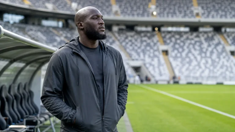 Romelu Lukaku in neutrale sportkleding aan de rand van een voetbalveld.