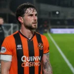 Will Ferry in een oranje-zwart voetbalshirt op een verlicht voetbalveld.