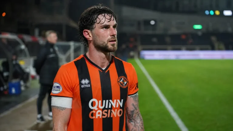 Will Ferry in een oranje-zwart voetbalshirt op een verlicht voetbalveld.