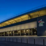 De buitenzijde van een voetbalstadion met een vaste OHL-signalisatie aan de gevel.