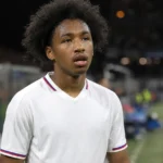 Malick Fofana in een wit voetbalshirt in een stadionomgeving.