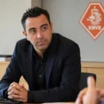 Xavi Hernández tijdens een gesprek aan een vergadertafel met een discreet KNVB-logo op de wand.