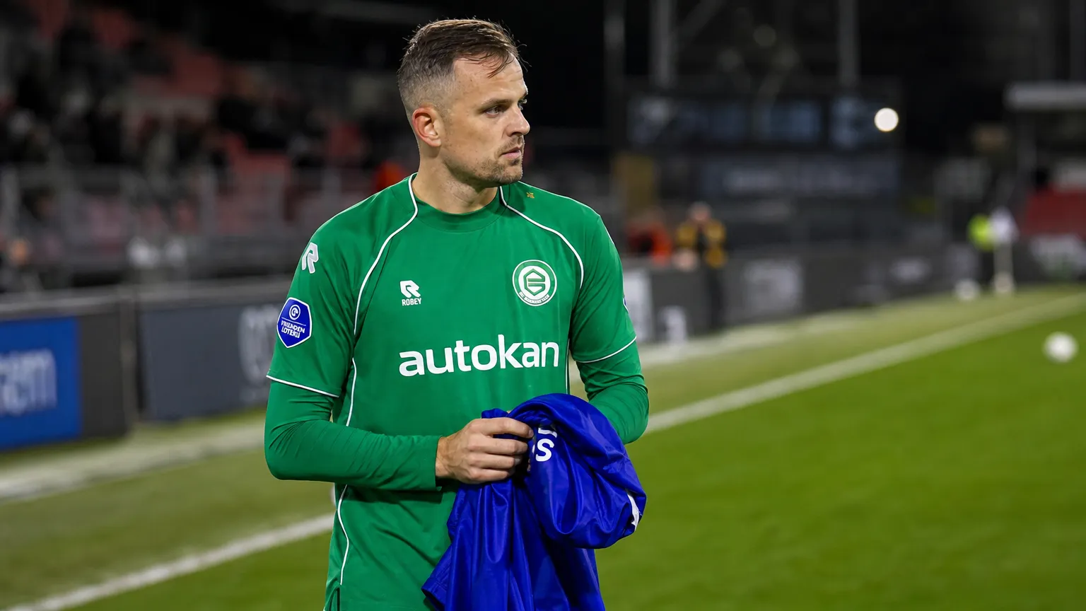 Mats Seuntjens in groen sportshirt langs de zijlijn van een voetbalveld.
