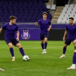 Voetballers in paarse shirts bouwen rustig op in een voetbalstadion met een discreet bord van RSC Anderlecht.